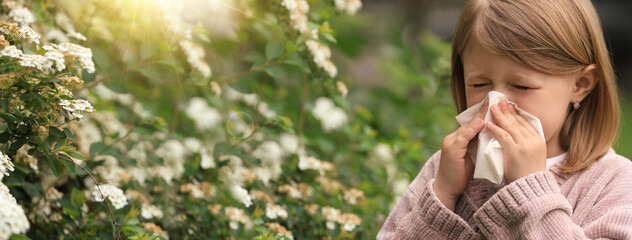 Little girl suffering from seasonal pollen allergy near blossoming tree on spring day. Banner...