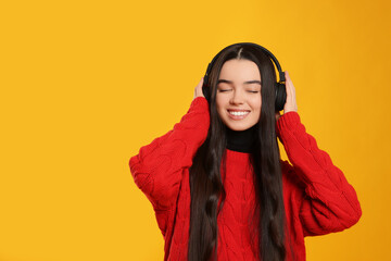 Teenage girl listening music with headphones on yellow background. Space for text
