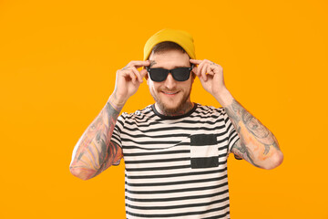 Handsome hipster man wearing stylish sunglasses on orange background
