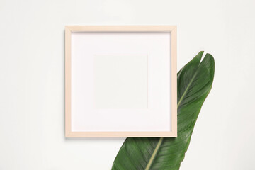 Empty photo frame and green leaf on white background, top view. Space for design