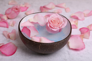Obraz na płótnie Canvas Beautiful composition with bowl of water and rose petals on light table, closeup. Spa treatment