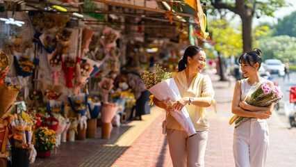 Happy Asian family mother and daughter holding flower bouquet walking together during shopping at florist shop street market in the city for flowers vase arrangement on spring summer holiday vacation.