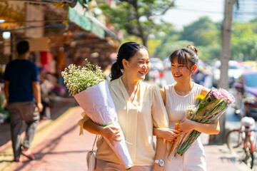 Happy Asian family mother and daughter holding flower bouquet walking together during shopping at...
