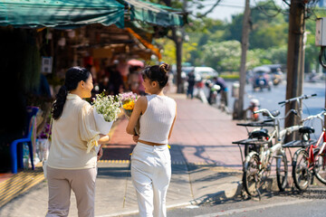 Happy Asian family mother and daughter holding flower bouquet walking crossing city street crosswalk during shopping at florist shop street market in the city on spring summer holiday vacation.