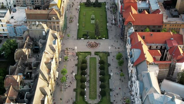 Aerial drone view of Timisoara at sunset, Romania. View of the Victory Square with multiple walking people and historical buildings around, Orthodox Cathedral