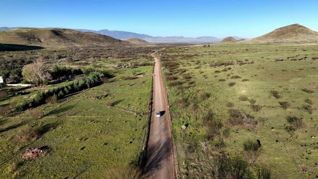 Aerial shot of car on dirt road in Willcox, Arizona, wide tracking drone shot with mountains in the background with dust trails