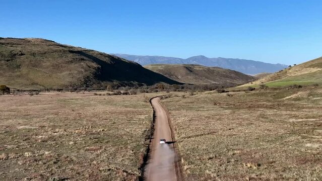 Aerial shot of car driving on dirt road in Willcox, Arizona, wide drone shot with mountains in the background
