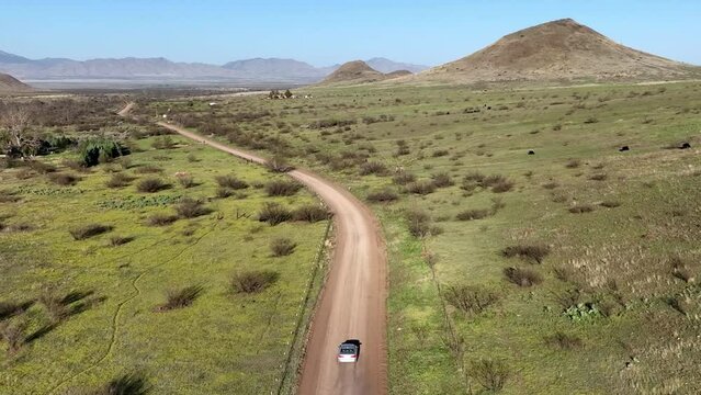 Aerial shot of car on dirt road in Willcox, Arizona, wide tracking drone shot with mountains in the background