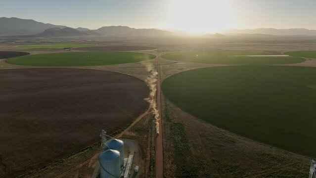 Drone shot of car driving on dirt road in near pivots with green farm growth in Willcox, Arizona, wide  aerial shot