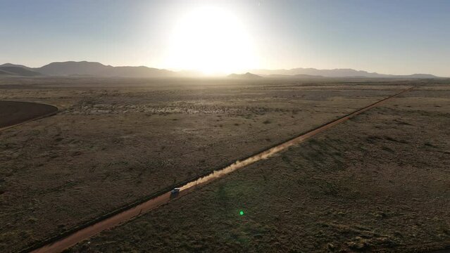 Aerial shot of car driving on dirt road in Willcox, Arizona, wide drone shot with mountains in the background and dust behind car