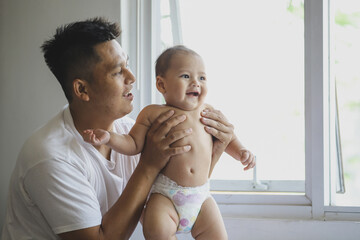 Proud and loving father holding his newborn baby near window in his home. Father's Day and fatherhood concept. - obrazy, fototapety, plakaty