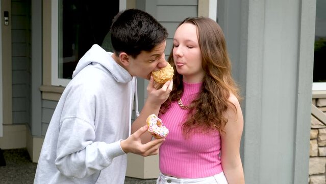 girl and boy tasting delicious desserts guy biting a donut biting off a bigger piece from a girl than at home teenagers on the street chatting couple young people in love adolescence