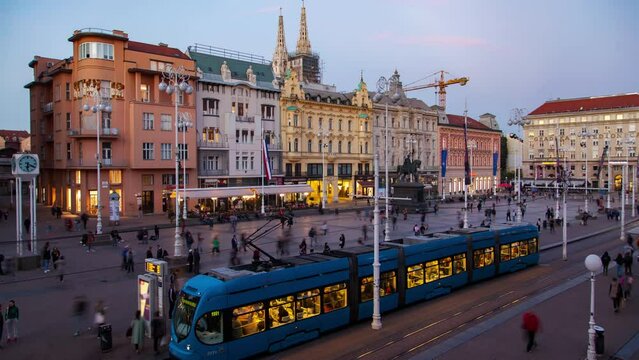 In this timelapse, the bustling Ban Jelacic Square in Zagreb, Croatia comes to life with fast-paced trams, people, and clouds during a captivating autumn sunset.