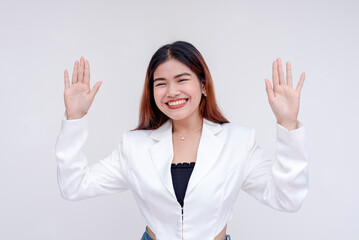 A smiling and cheerful young woman with both arms raised in surrender. Isolated on a white background.