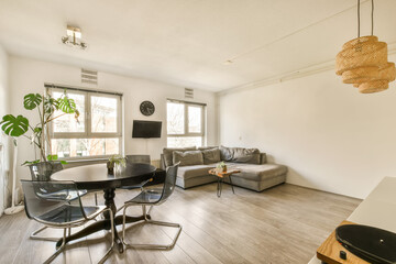 a living room with wood flooring and white walls, there is a small dining table in front of the couch