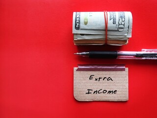 On copy space red background, cash dollars money with pen writing on note EXTRA INCOME, concept of make more income from side business or second job along to boost extra cash