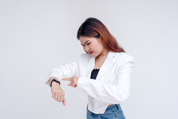 An impatient and angry young woman pointing and looking at her watch. Isolated on a white background. - obrazy, fototapety, plakaty