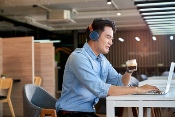 Asian male drink a cup of coffee with bitter taste and disgust face and use laptop for business.