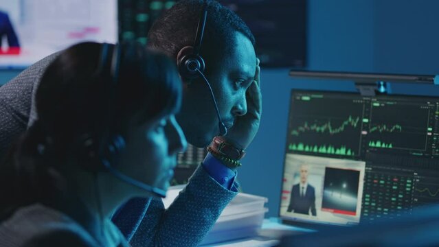 Mixed race stock traders work on PC with real-time stocks in broker agency office at night. Big screen with TV news broadcast and exchange market charts. Cryptocurrency trading and analytics. Close up
