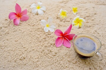 Cup coffee and plumeria flowers on the sand