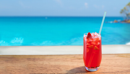 glass of cold strawberry soda juice on wood table over blue sea background