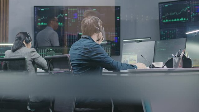 Diverse stock traders monitor real-time stocks data on computers, work in broker agency office. Colleagues watch exchange market charts on big digital screens. Cryptocurrency trading and investment.