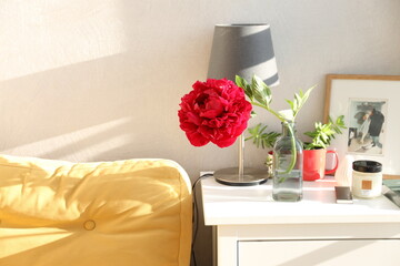 Red peony in a glass bottle on the bedside table near the sofa