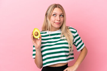 Young caucasian woman holding an avocado isolated on pink background having doubts and thinking