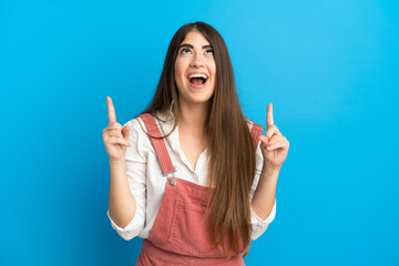 Young caucasian woman isolated on blue background surprised and pointing up