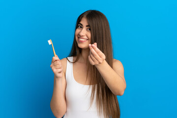 Young caucasian woman brushing teeth isolated on blue background making money gesture