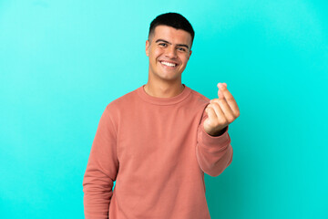 Young handsome man over isolated blue background making money gesture