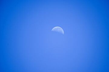 A faintly visible crescent moon in the late afternoon sky.