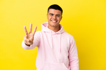 Fototapeta premium Young handsome man over isolated yellow background happy and counting three with fingers
