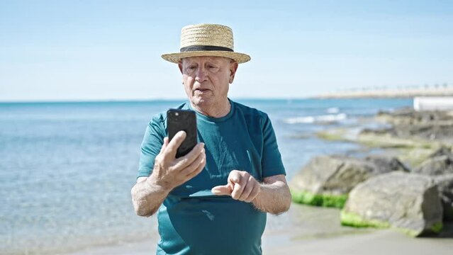 Senior grey-haired man tourist wearing summer hat make selfie by smartphone at seaside