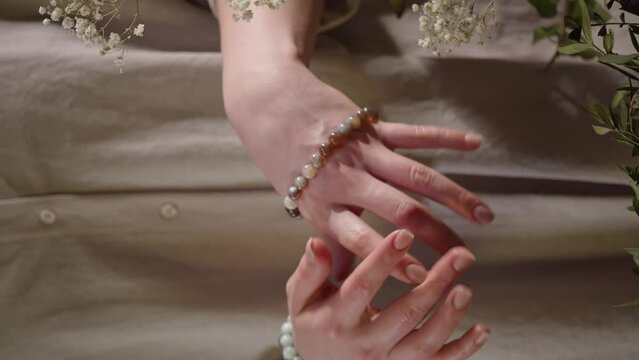 A woman in a beige shirt wears a bracelet made of stones on her arm. Vertical shot of women's hands in stone bracelets, natural crystals in jewelry