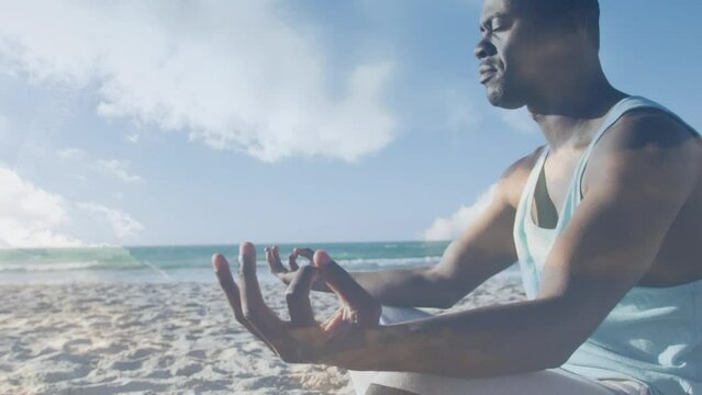 Animation of clouds over exercising african american man doing yoga on beach