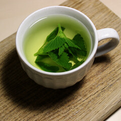 Hot mint tea in a white cup on a wooden desk closeup photo 
