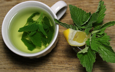  Freshly brewed melissa leaves in a cup on a wooden surface with bunch of green melissa leaves and lemon slice 
