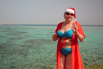 Funny senior woman in santa claus hats and sunglasses wearing in swimsuit on the sea beach, women...
