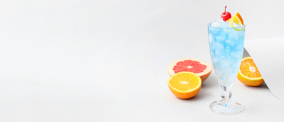 Glass of Blue Lagoon cocktail and citrus fruits on light background with space for text
