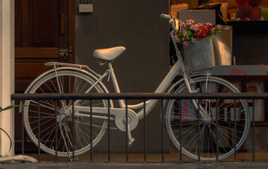 A white bicycle with a cart full of colorful flowers, in a corner of the cafe with warm vintage yellow. Decorative bicycle concept. Vintage photo.
