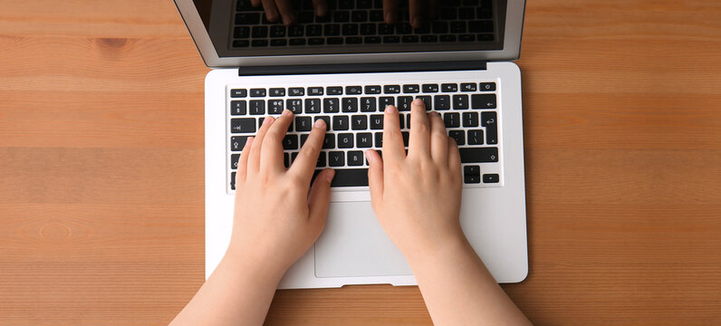 Hands of programmer and laptop on wooden background, top view