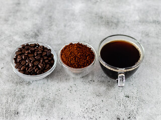 Close shot of coffee beans, ground powder and cup of americano over white background.