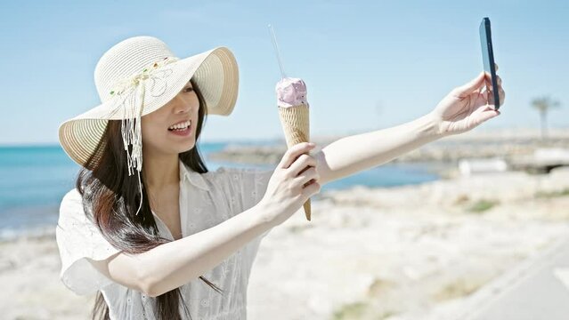 Young chinese woman tourist having video call eating ice cream at seaside