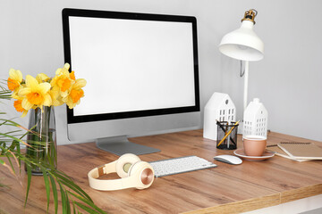 Modern PC, headphones, narcissus flowers and coffee on wooden table near light wall