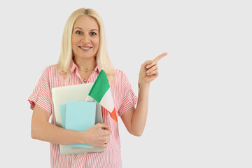 Mature woman with flag of Italy, books and laptop pointing at something on white background