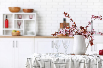 Vase with blooming tree branches, apple and glasses on table in kitchen
