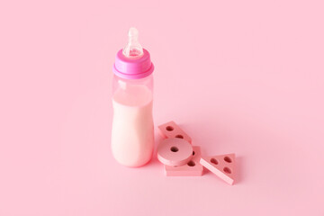 Bottle of milk for baby with toys on pink background