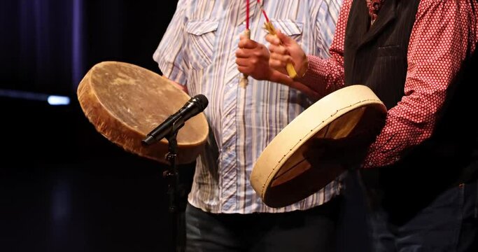A close up to a couple of people playing Canadian native indigenous drums.