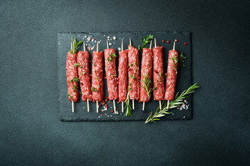 Lula kebab on skewers with spices in a black slate board on a stone background. Top view.